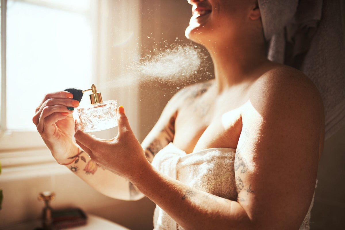 A smiling woman in a towel spraying scent in a bright bathroom
