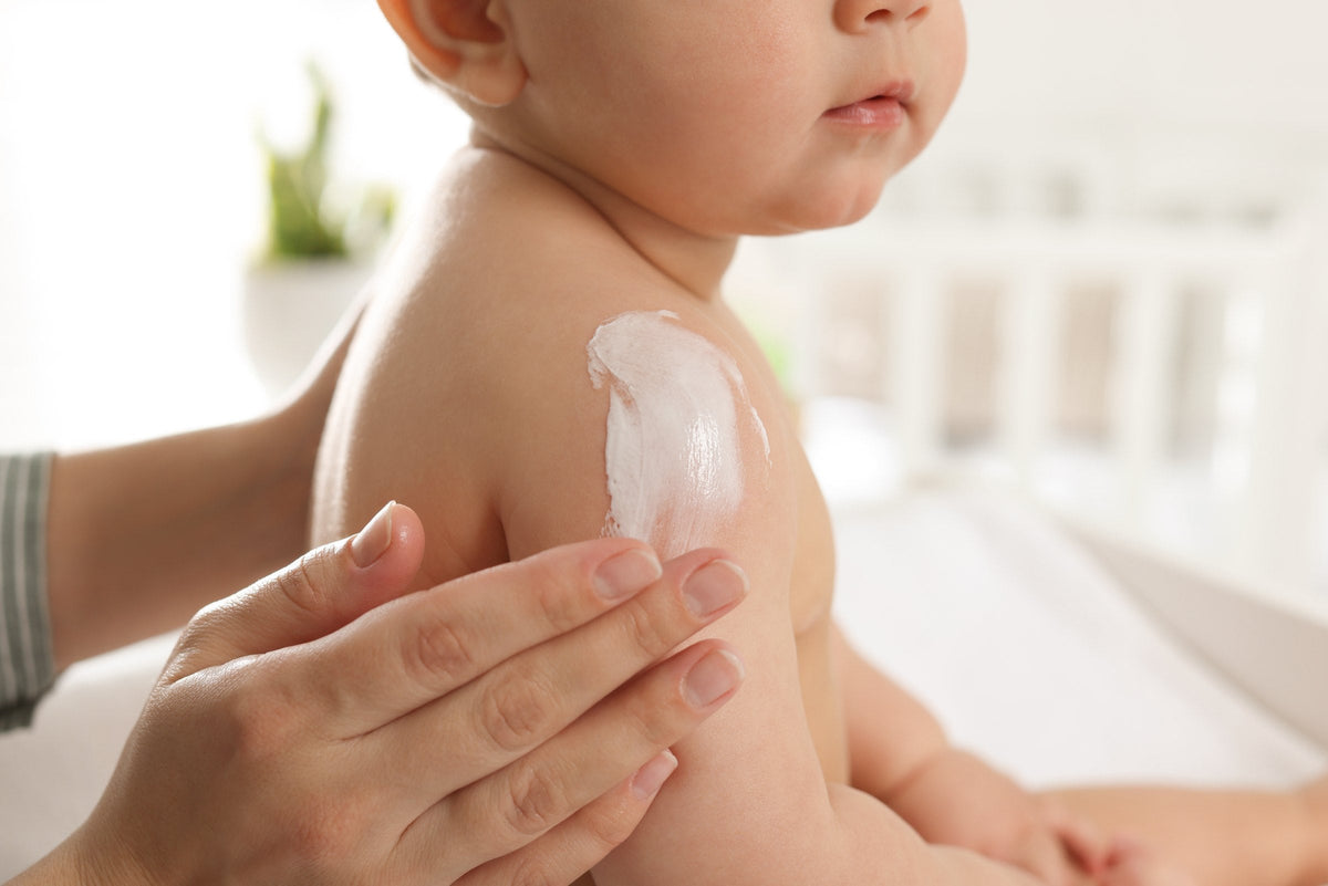 A mother gently applying body cream to her baby at home