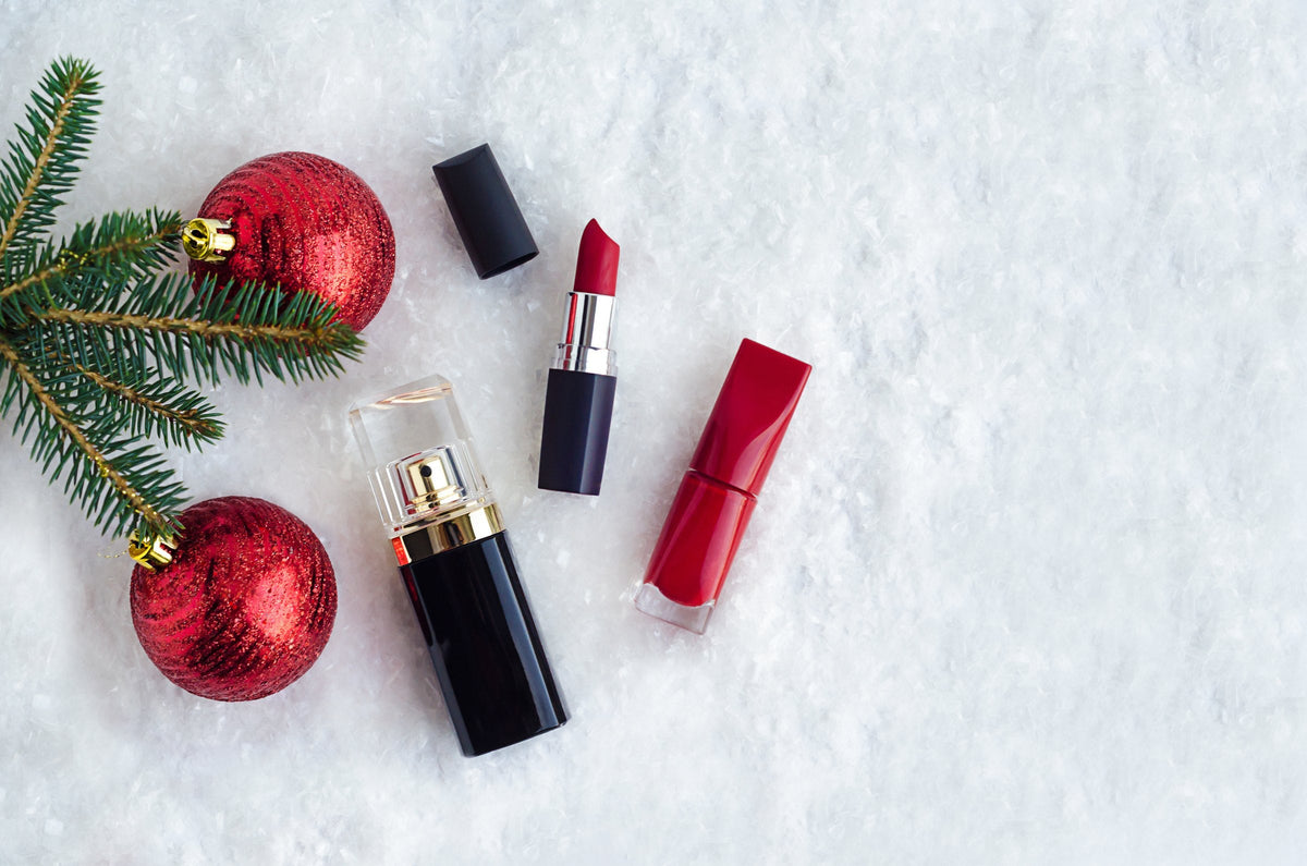 Red lipstick, nail polish and perfume under a spruce branch